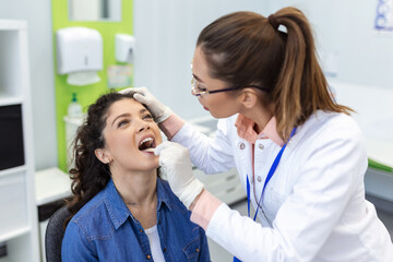 Doctor using inspection spatula to examine patient throat. ENT doctor doing throat exam of a woman. patient opened her mouth to throat check-up