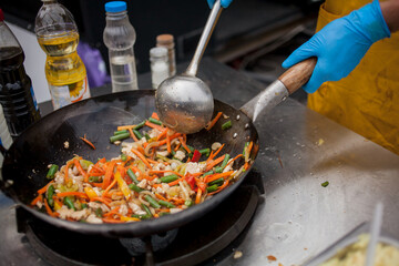 cook fries vegetables in a wok pan on fire. Chef is stirring vegetables in wok. Chef cooking with...