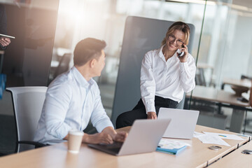 mature business woman sitting on table and talking phone with client during meeting in office 