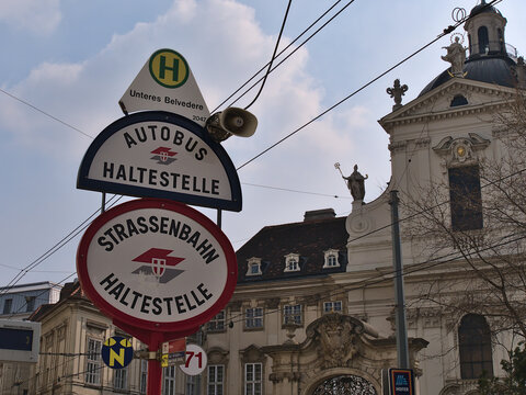 Street signs at bus and tram station Unteres Belvedere in the historic downtown of Vienna, Austria with the logo of Wiener Linien and old building.