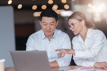 Two diverse business people focused while working on a laptop together at boardroom table in office.