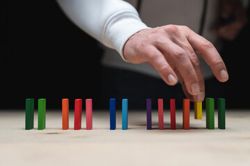 Conceptual photo of a hand placing a stone to a row of domino stones.
Domino effect with colored...