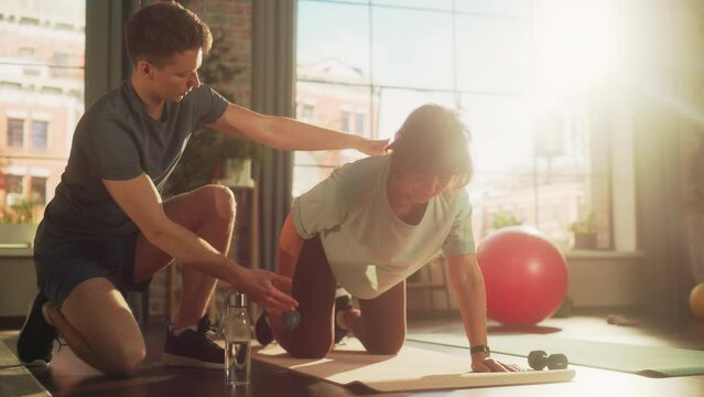 Middle Aged Woman Exercising at Home with Personal Trainer. Elderly Female Strengthening Core and Arm Muscles with Dumbbell Workout. Young Athlete Supporting and Guiding Her Through the Training.