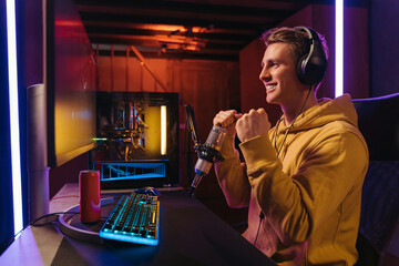 Winner pro gamer celebrating his victory. Guy cyber sportsman streaming while playing shooter video games at home, feels happy with victory in online cyber sport tournament. Neon color. Side view. © Arsenii