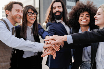 Multiethnic business people stacking hands with colleagues outdoor with city on background - Focus on top arm