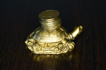 Metal turtle with coins on a dark background. A financial symbol of well-being and stability.
