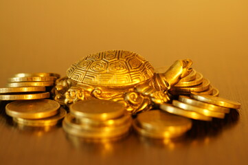 Metal turtle with coins on a gold background. A financial symbol of well-being and stability.