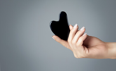 Female hand with obsidian gua sha over grey background with copy space. Anti aging beauty and...