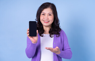 Portrait of middle aged Asian woman using smartphone on blue background