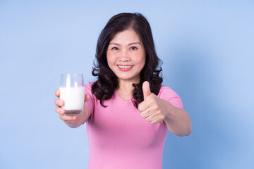 Image of middle aged Asian woman drinking milk on blue background