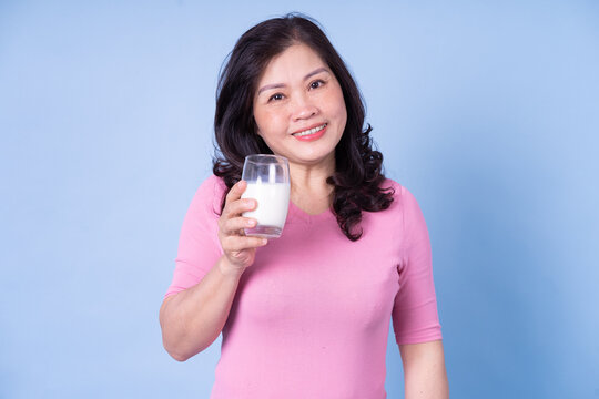 Image Of Middle Aged Asian Woman Drinking Milk On Blue Background