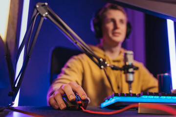Closeup of pro gamer's hands on computer mouse and keyboard in neon color, blur background. Professional cyber sport gamer streaming his play online at home. Close up, selective focus on his hand