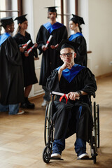 Full length portrait of young man with disability at graduation ceremony in university