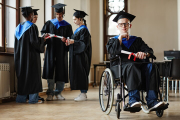 Full length portrait of young man with disability at graduation ceremony in university, copy space