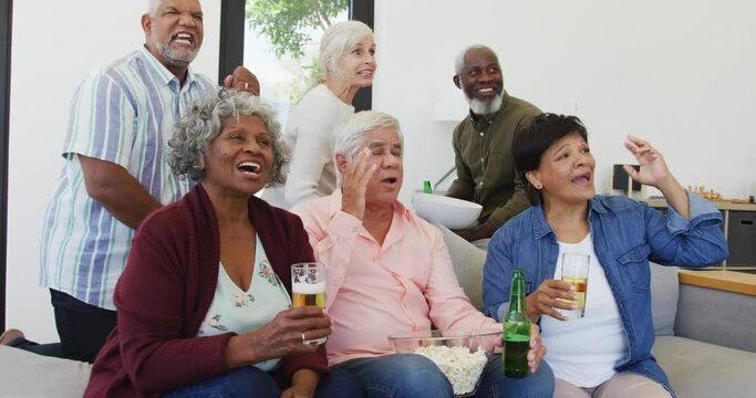 Happy senior diverse people watching tv with beer at retirement home