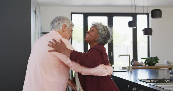 Happy senior diverse couple dancing in kitchen at retirement home