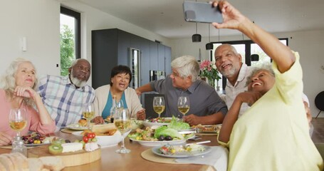 Happy senior diverse people having dinner and taking selfie at retirement home