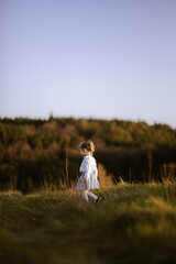 Dziewczynka spacerująca po łące przy zachodzie słońca - obrazy, fototapety, plakaty