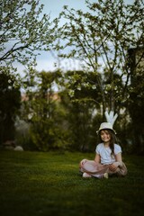Dziewczynka siedzi na trawce przy drzewach jabłoni