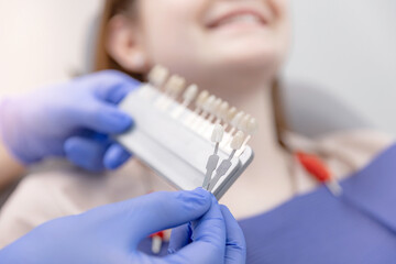 Woman client chooses color of whitening or veneers teeth at dentist appointment