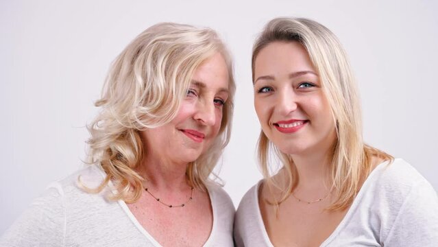 Close-up studio shot of a mother and daughter looking at each other with love and trust, smiling, touching their heads. High quality 4k footage