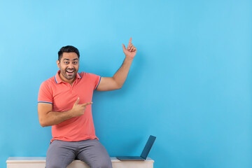 Cheerful young man pointing elsewhere while using laptop
