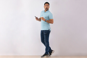 Portrait of a surprised young man standing with Smartphone and Coffee against white background
