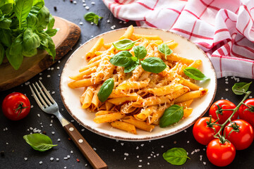 Pasta with tomato sauce, basil and parmesan on dark table. Penne pasta with tomato sauce alla arrabbiata.