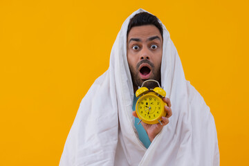 Portrait of a shocked young man holding alarm clock over yellow background
