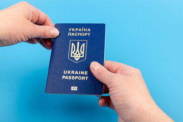 Passport of a citizen of Ukraine in a female hand on a blue background, close-up. Inscription in Ukrainian Ukraine Passport