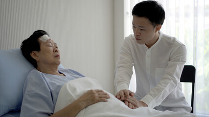 Fototapeta premium Asian family adult son worry take care of ill elderly mother admit sleeping in hospital bed