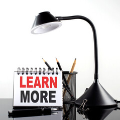 LEARN MORE text on notebook with pen and table lamp on the black background