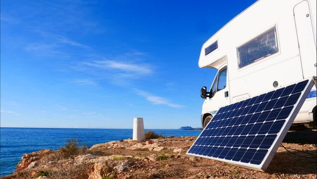 Time lapse of clouds moving across sky over portable solar panel at camper vehicle on sea coast. Renewable free energy on caravan vacation.