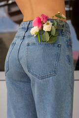 Woman with beautiful tender flowers in back pocket of jeans. Woman stabs back to camera. A tiny bouquet of field flowers in a back pocket.