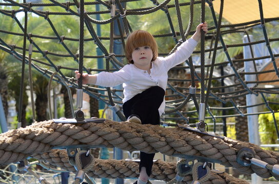 Happy boy cheering while climbing a net. Child crawling on rope mesh at playground