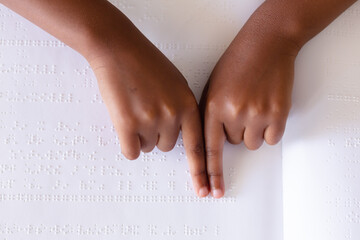 Cropped hands of african american elementary schoolgirl studying while touching braille book