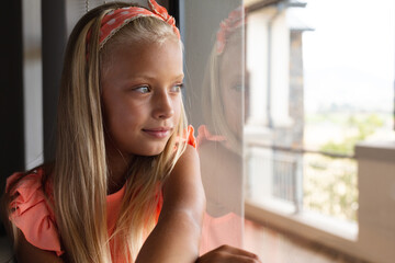 Caucasian elementary schoolgirl leaning on glass window in classroom