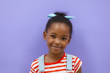 Portrait of smiling african americana elementary schoolgirl against purple background
