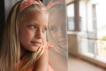 Close-up of caucasian elementary schoolgirl leaning on glass window in classroom