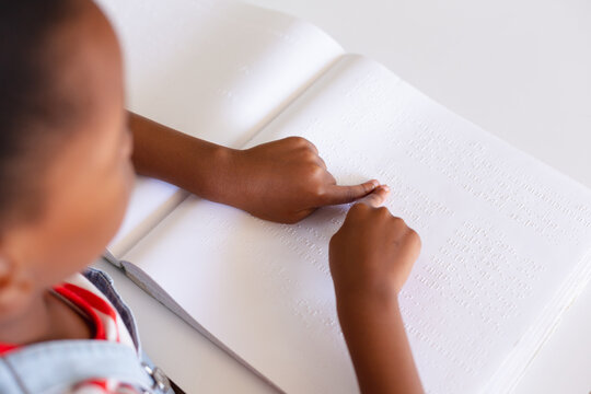 African american elementary schoolgirl touching braille book while studying at desk in class