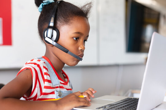 Close-up of african american elementary schoolgirl wearing headphones while using laptop at desk