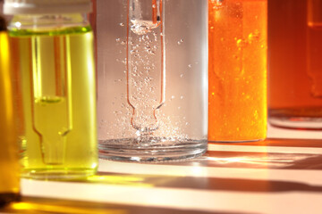 Different cosmetic glass bottles standing in a row on light background. Macro. Soft focus. Abstract colorful pattern in the sunlight. Red, green and yellow shades. Front view with copy space