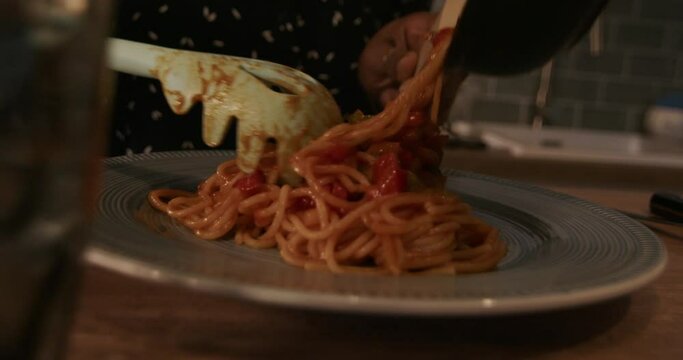 Woman standing by table with frying pan putting spaghetti on plate