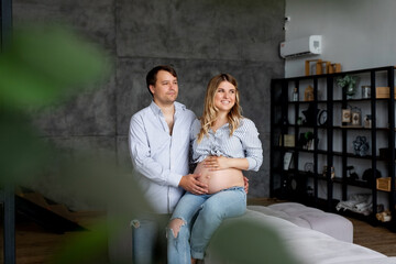 Photo of joyful young man and pregnant woman couple wait baby touch belly sit sofa indoors living...
