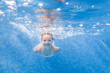 Little child girl swimming underwater in the paddling pool. Diving. Learning infant child to swim....