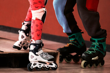Fototapeta premium Two pairs of roller skates close-up in the rolling room. The coach teaches the child to roller-skate indoors. Overcome obstacles.