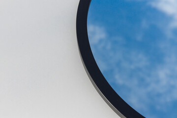 A round or oval mirror with a reflection of the blue sky and white clouds. Close-up. Isolated on a white background