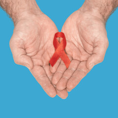 Red awareness ribbon bow on mans helping hands isolated on blue background. HIV, AIDS world day. Social life issues concept. Aids charity fund concept. Healthcare and medicine concept