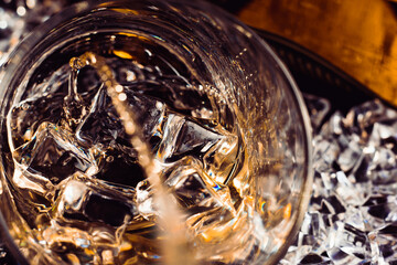 closeup of an amber whiskey glass with ice cubes and splashing as it fills