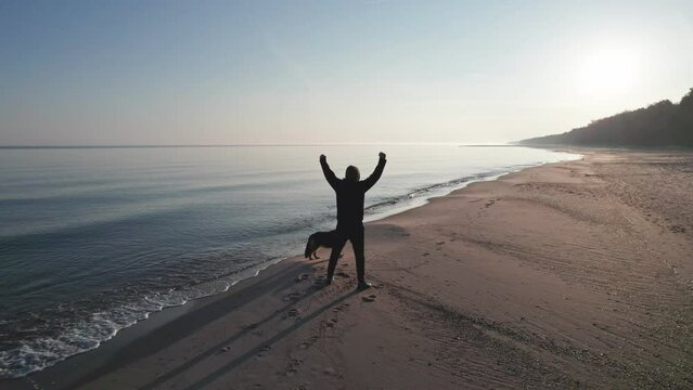 A dressed man enjoys his faithful dog on an empty beach at sunrise. Friendship between man and animal.
